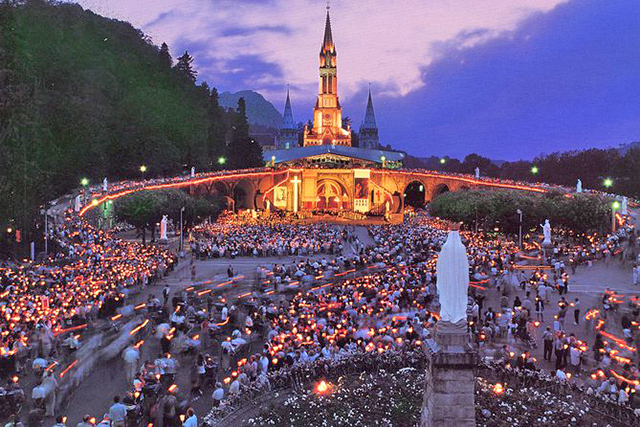 Het plein voor de basiliek in Lourdes, 's avonds vol mensen.