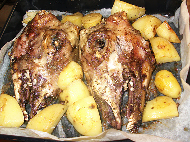Twee lamskoppen in een ovenschotel met aardappelen.