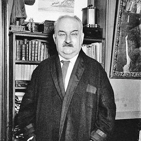 Een foto van Curnonsky, staand voor een boekenkast.