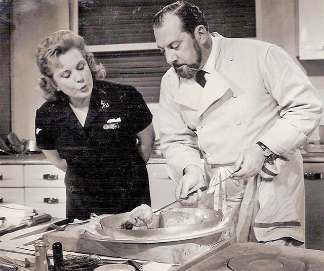 Oliver aan het werk in een keuken, terwijl een vrouw toekijkt.