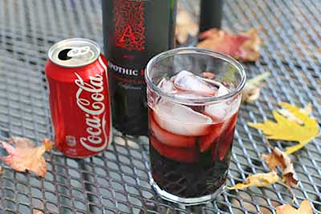 Een blikje cola, een fles rode wijn, en een glas met kalimotxo.