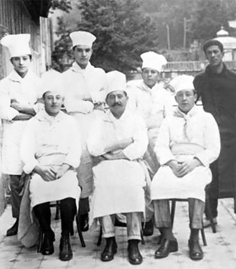 Een oude foto van een keukenbrigade, met zes koks en een stoker.
