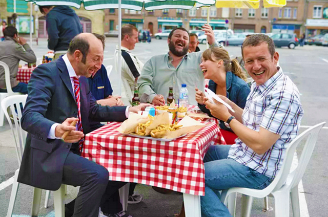Een scène uit de film, waarop men vrolijk luncht aan een terras-tafeltje.
