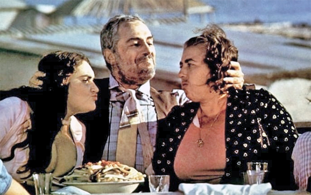 Een scène uit de film. De hoofdrolspeler aan tafel met aan de ene kant zijn vrouw en aan de andere kant zijn geliefde.