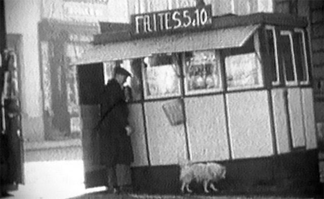 Een man met een hondje bij een frietkot waarop staat 'Frites 5,10.